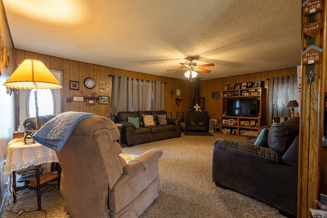 carpeted living room with a wood stove, wooden walls, a textured ceiling, and ceiling fan