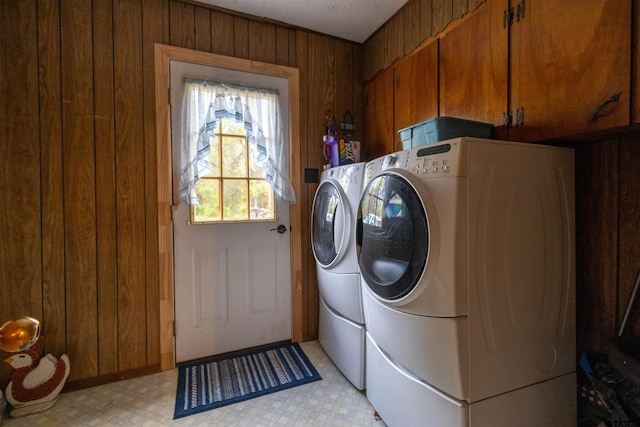 clothes washing area featuring cabinets, wooden walls, and washer and clothes dryer