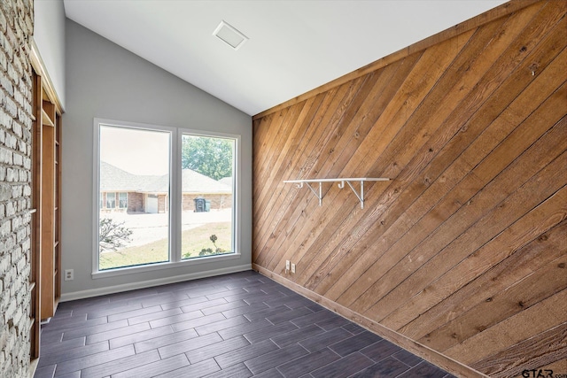 unfurnished room with wooden walls and vaulted ceiling