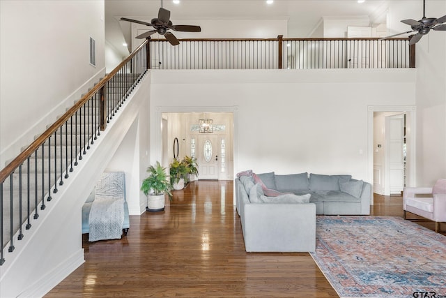 living room with ceiling fan, dark hardwood / wood-style flooring, a towering ceiling, and ornamental molding