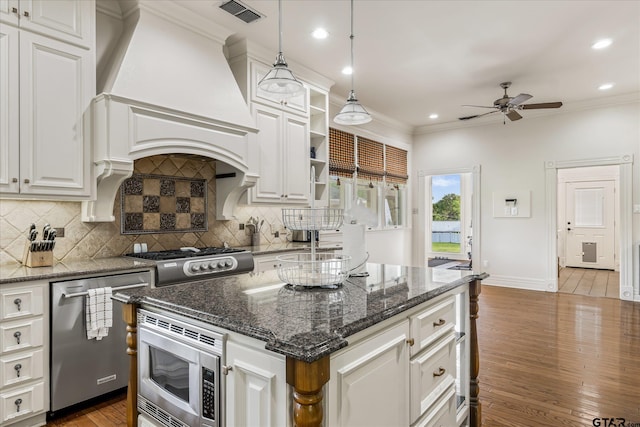 kitchen featuring premium range hood, white cabinetry, appliances with stainless steel finishes, decorative light fixtures, and a center island