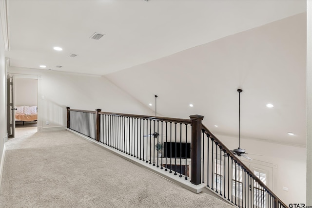 hallway with vaulted ceiling, ornamental molding, and light colored carpet