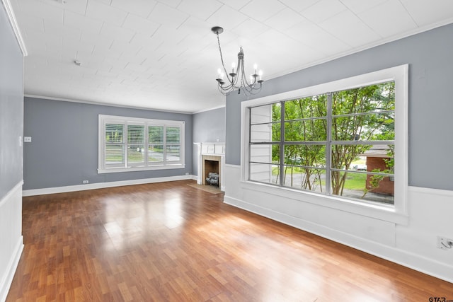 unfurnished living room with a fireplace with flush hearth, a chandelier, wood finished floors, and ornamental molding