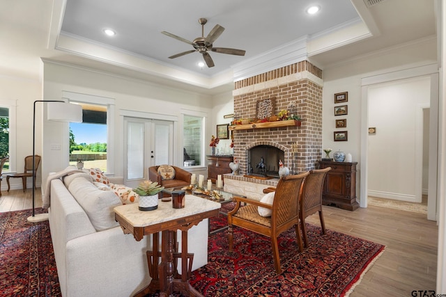 living room featuring light wood-type flooring, a raised ceiling, crown molding, and a fireplace