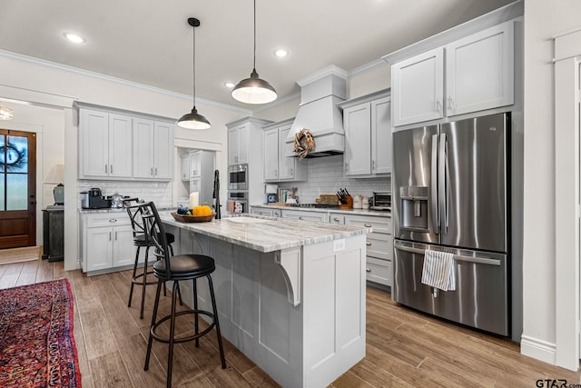 kitchen with light hardwood / wood-style flooring, custom exhaust hood, a kitchen island with sink, and stainless steel appliances