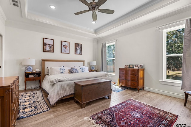 bedroom featuring a tray ceiling, multiple windows, ceiling fan, and light hardwood / wood-style flooring