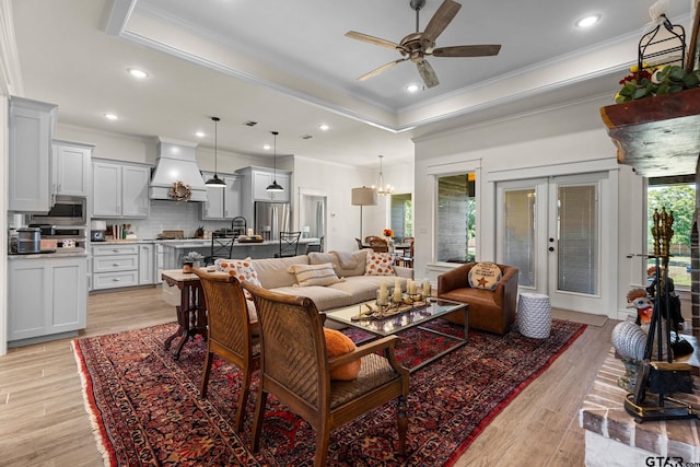 living room with light wood-type flooring, ceiling fan with notable chandelier, a raised ceiling, and crown molding