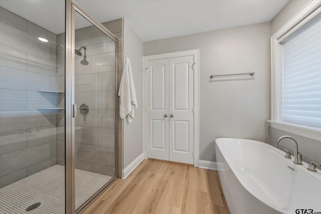 bathroom featuring a wealth of natural light, a freestanding tub, wood finished floors, a shower stall, and baseboards