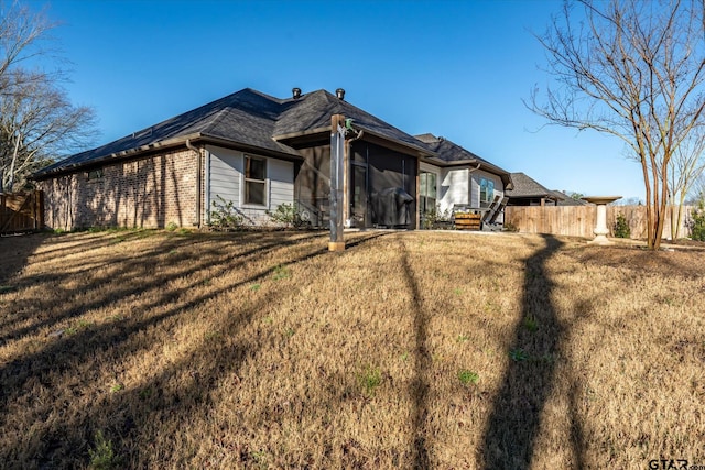 exterior space with a yard, fence, brick siding, and a sunroom