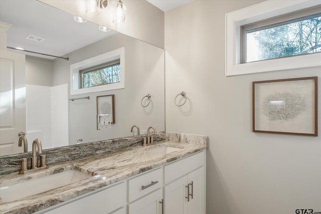 bathroom with double vanity, visible vents, a shower, and a sink