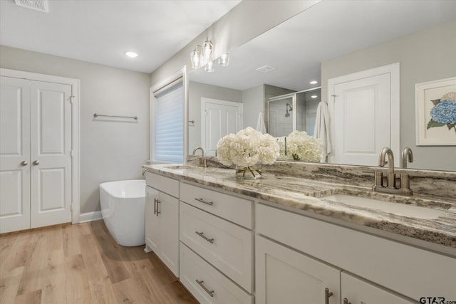 bathroom featuring double vanity, wood finished floors, a stall shower, and a sink