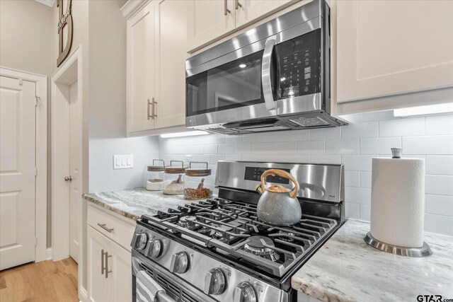 kitchen featuring light stone countertops, light wood-type flooring, backsplash, and stainless steel appliances