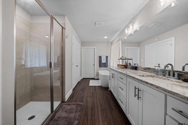 409 Meadow Ln, Chandler, TX 75758 - bathroom featuring double vanity, a shower stall, a freestanding bath, and wood finished floors