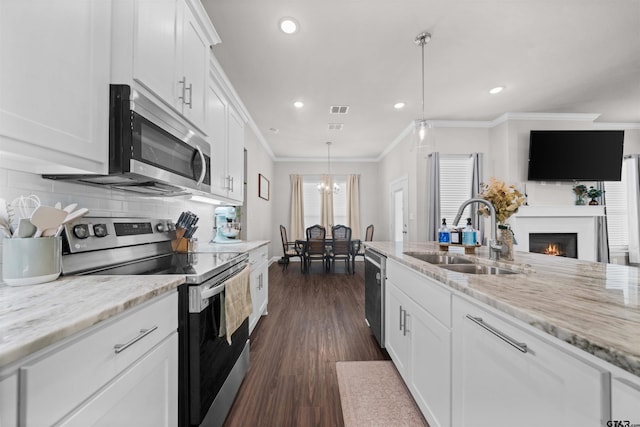 409 Meadow Ln, Chandler, TX 75758 - kitchen with stainless steel appliances, recessed lighting, a warm lit fireplace, white cabinetry, and crown molding