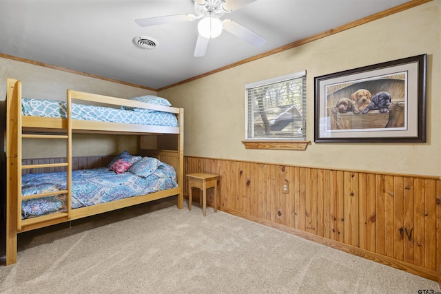 carpeted bedroom with wooden walls, visible vents, ornamental molding, and wainscoting