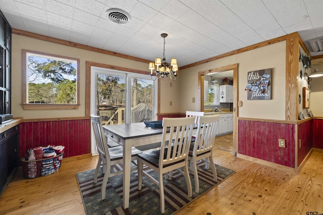 dining space with a wainscoted wall, visible vents, light wood finished floors, and an inviting chandelier