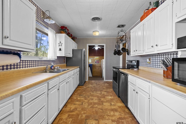 kitchen featuring stainless steel appliances, a sink, white cabinetry, visible vents, and wallpapered walls