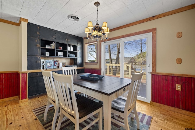 dining space featuring light wood-style floors, wainscoting, visible vents, and crown molding