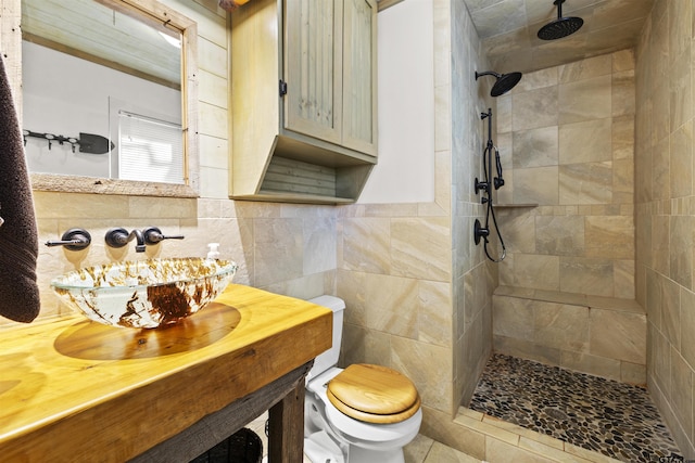 bathroom featuring tile walls, tiled shower, toilet, a wainscoted wall, and a sink