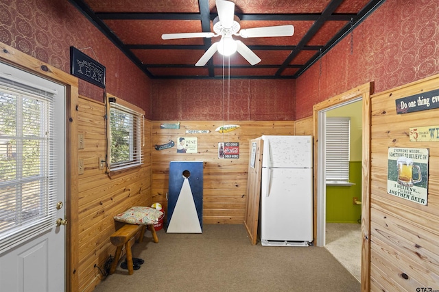 interior space with ceiling fan, wood walls, carpet, and freestanding refrigerator