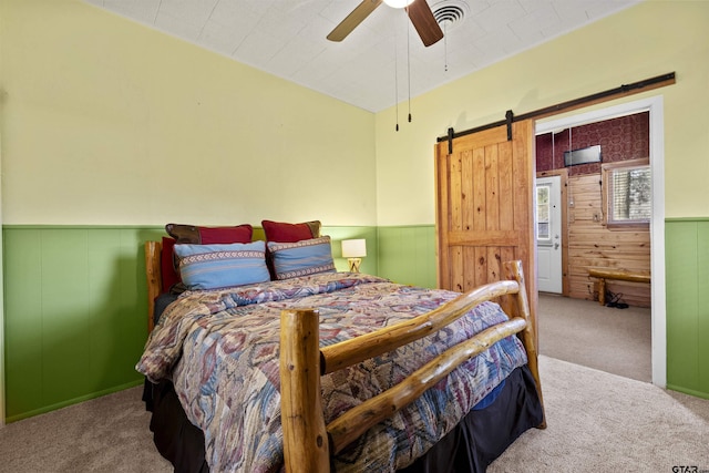 carpeted bedroom with wainscoting, ceiling fan, visible vents, and a barn door