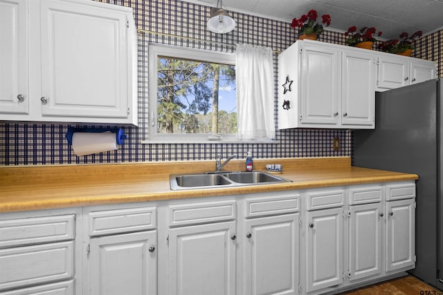 kitchen with freestanding refrigerator, white cabinets, light countertops, and a sink