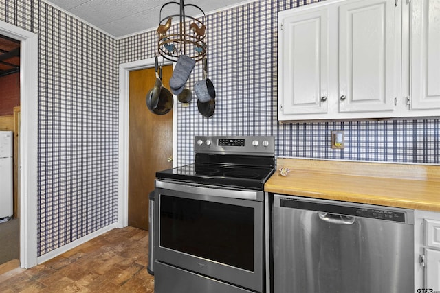 kitchen with wallpapered walls, baseboards, stainless steel appliances, light countertops, and white cabinetry