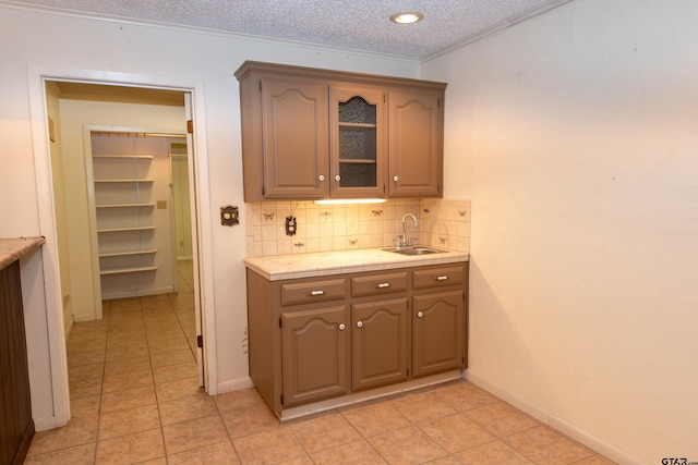 kitchen featuring decorative backsplash, sink, light tile patterned floors, and a textured ceiling