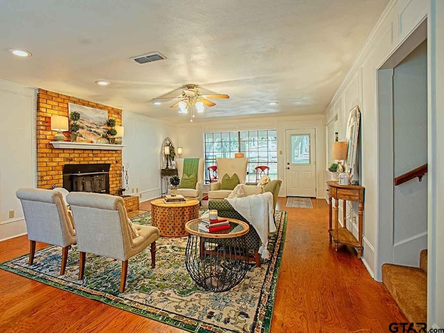 living room featuring a fireplace, hardwood / wood-style flooring, ceiling fan, and ornamental molding