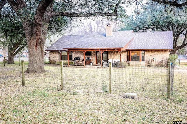 ranch-style house with fence private yard, brick siding, a front yard, and roof with shingles