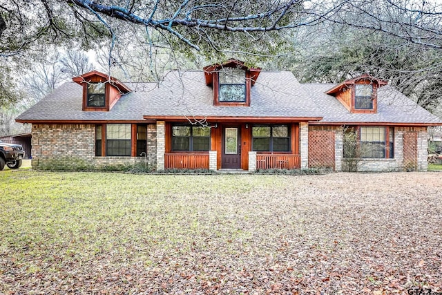 view of front facade featuring a porch, roof with shingles, brick siding, and a front lawn