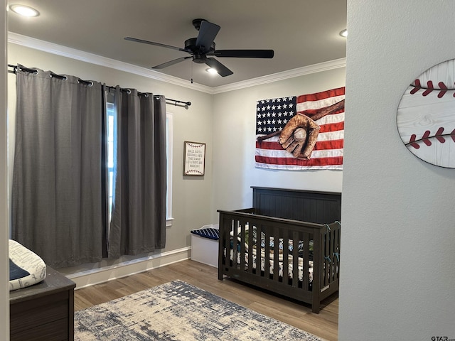 bedroom featuring a ceiling fan, a nursery area, wood finished floors, and crown molding