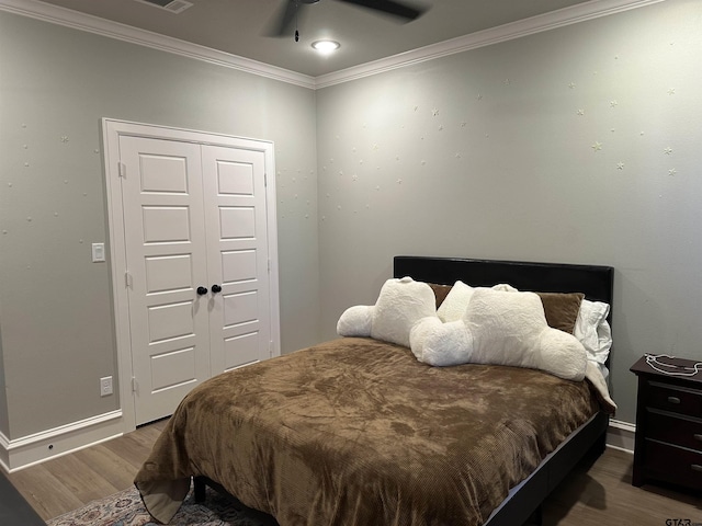 bedroom with crown molding, ceiling fan, baseboards, wood finished floors, and a closet