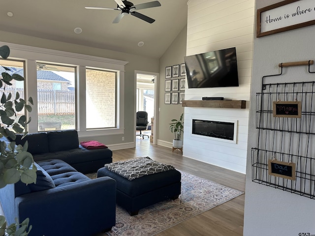 living room featuring wood finished floors, baseboards, a fireplace, ceiling fan, and vaulted ceiling