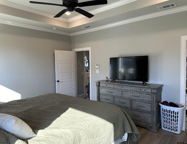 bedroom with a tray ceiling, visible vents, wood finished floors, and crown molding