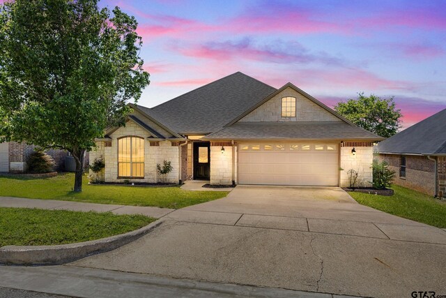 traditional-style house featuring a shingled roof, a front lawn, driveway, stone siding, and a garage