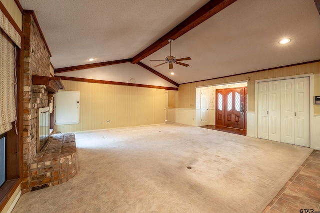 unfurnished living room with carpet flooring, ceiling fan, vaulted ceiling with beams, a textured ceiling, and a large fireplace