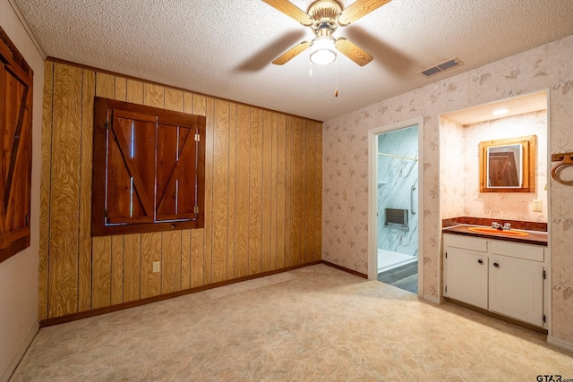 carpeted spare room with ceiling fan, wood walls, sink, and a textured ceiling