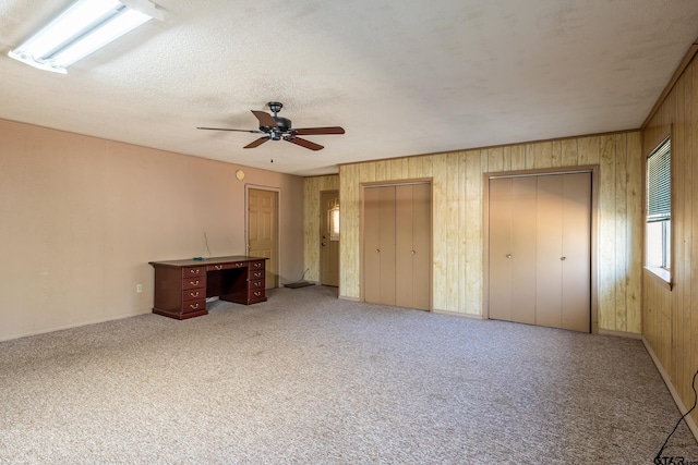 unfurnished bedroom featuring carpet, wood walls, two closets, ceiling fan, and a textured ceiling