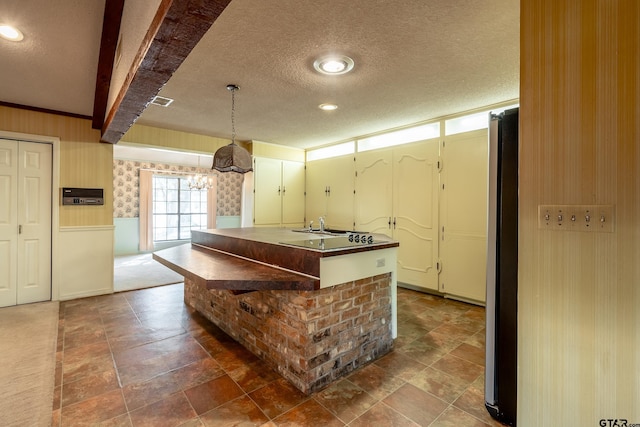 kitchen with a textured ceiling, decorative light fixtures, stainless steel refrigerator, and a notable chandelier