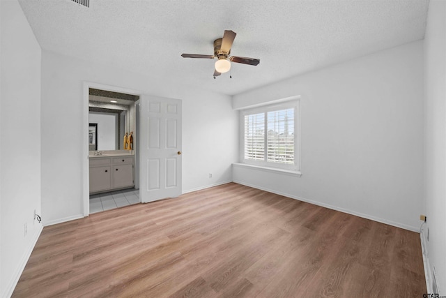 unfurnished bedroom featuring a textured ceiling, light hardwood / wood-style floors, ensuite bath, and ceiling fan