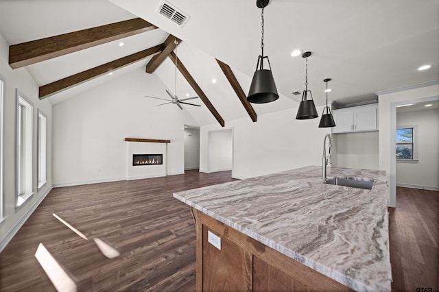 kitchen featuring beam ceiling, white cabinetry, sink, light stone countertops, and decorative light fixtures