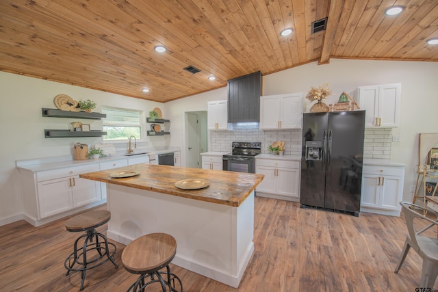 kitchen with black appliances, vaulted ceiling with beams, a kitchen island, white cabinetry, and light hardwood / wood-style floors