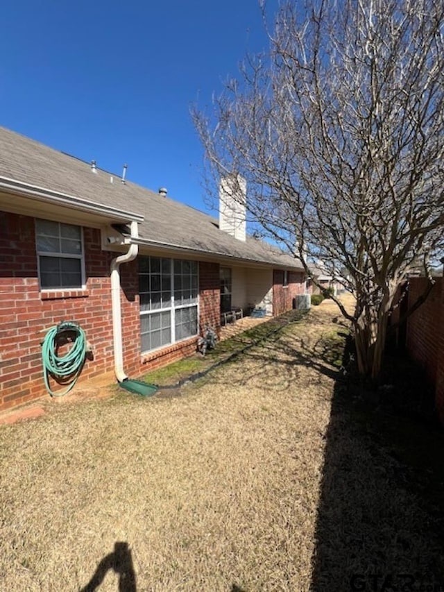 view of side of home with brick siding, a lawn, a chimney, and fence