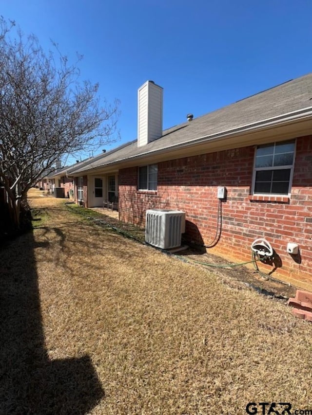 back of house with brick siding, central AC unit, a chimney, and a yard