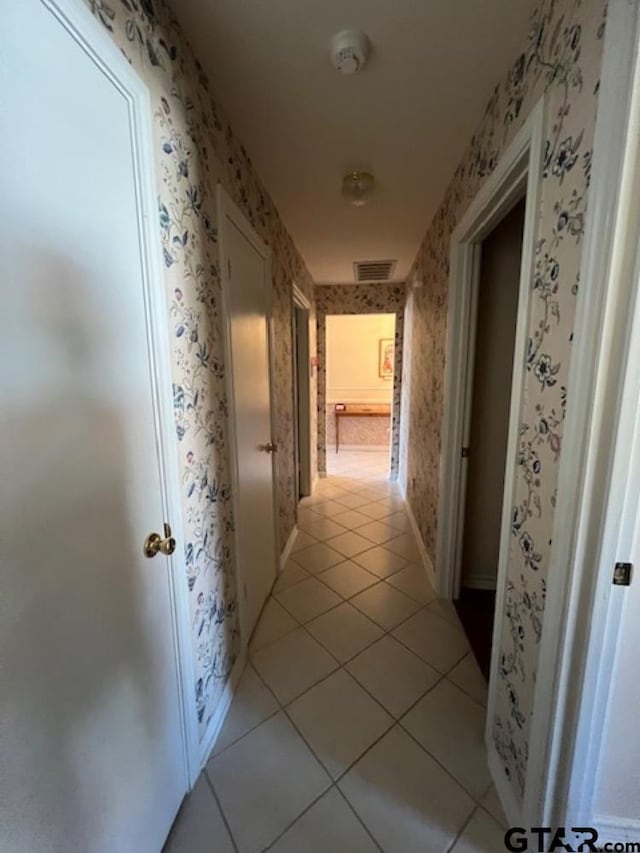 hallway with light tile patterned floors, visible vents, wallpapered walls, and baseboards