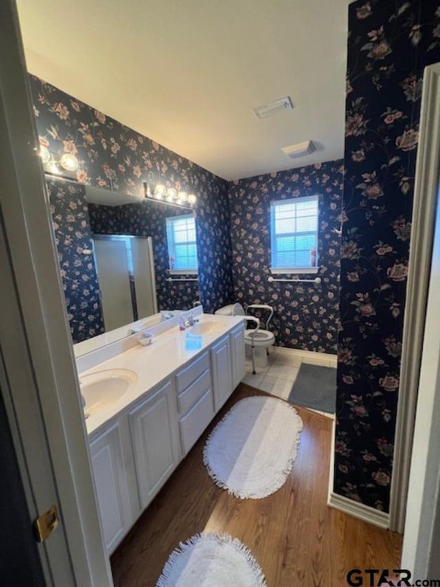 bathroom featuring a sink, wood finished floors, a bidet, wallpapered walls, and double vanity