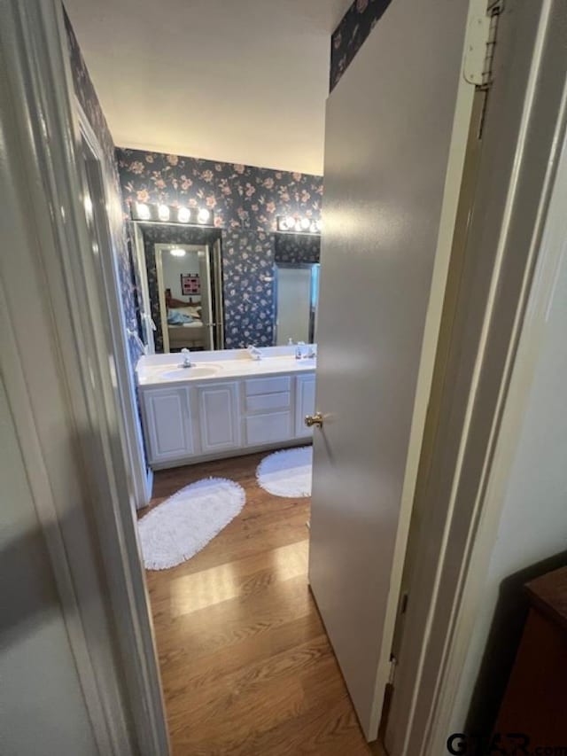 bathroom featuring wallpapered walls, double vanity, wood finished floors, and a sink