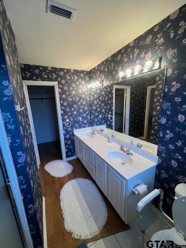 full bathroom with wallpapered walls, toilet, visible vents, and a sink