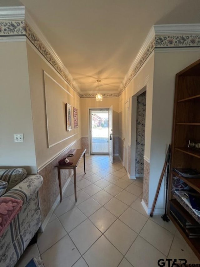 hall with a notable chandelier, light tile patterned floors, a wainscoted wall, and ornamental molding